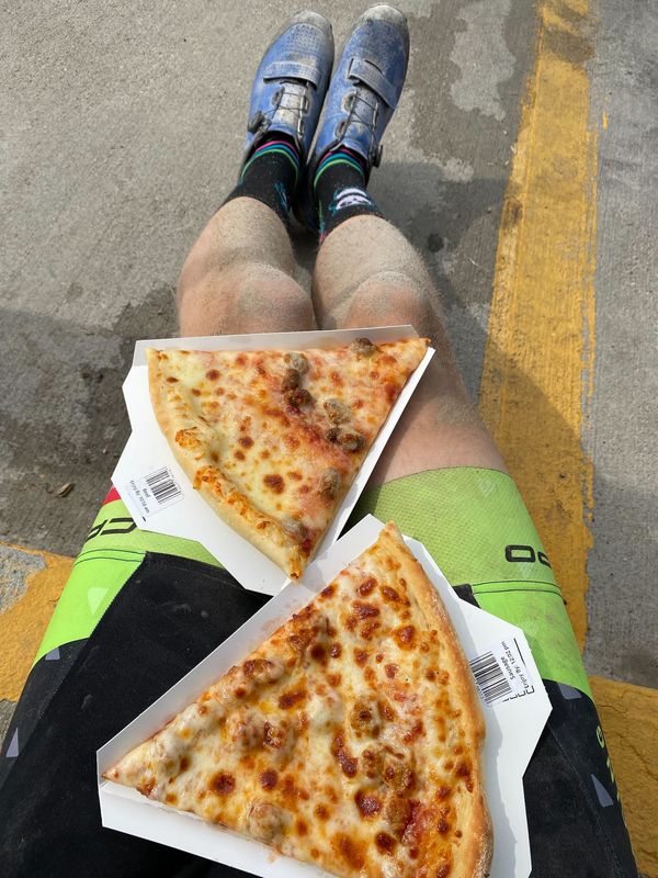 A pair of dirty legs, eating slices of pre-made pizza