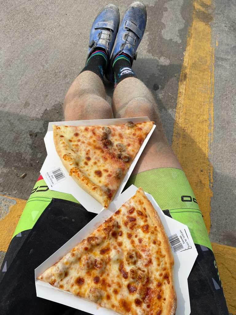 A pair of dirty legs, eating slices of pre-made pizza